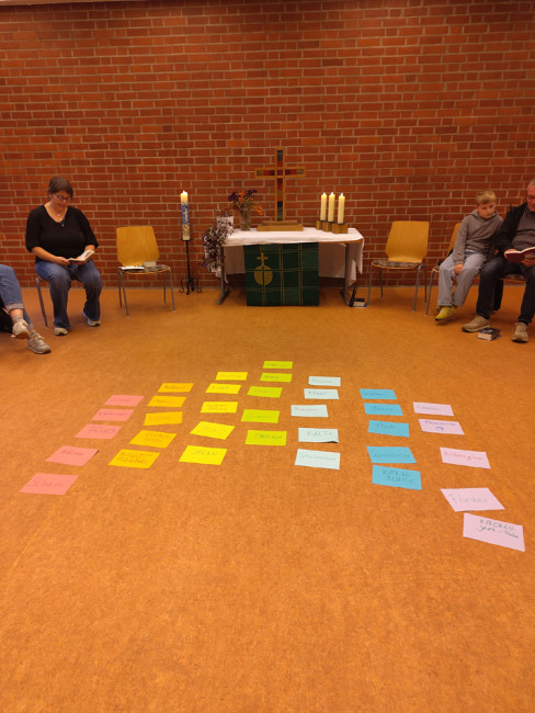 Gedanken zu den Farben des Regenbogens auf buntem Papier auf dem Boden, dahinter der Altar im Gemeindehaus der Erlöserkichrche.