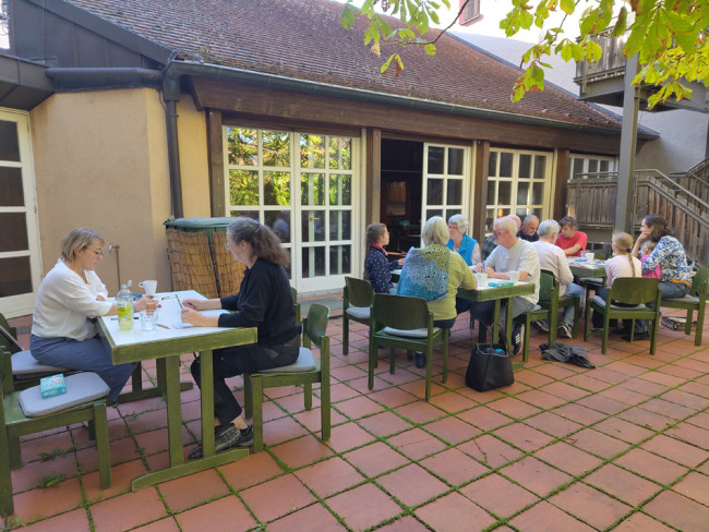 Die Mitspieler:innen an den Tischen beim Spielenachmittag auf der Terrasse des Remters